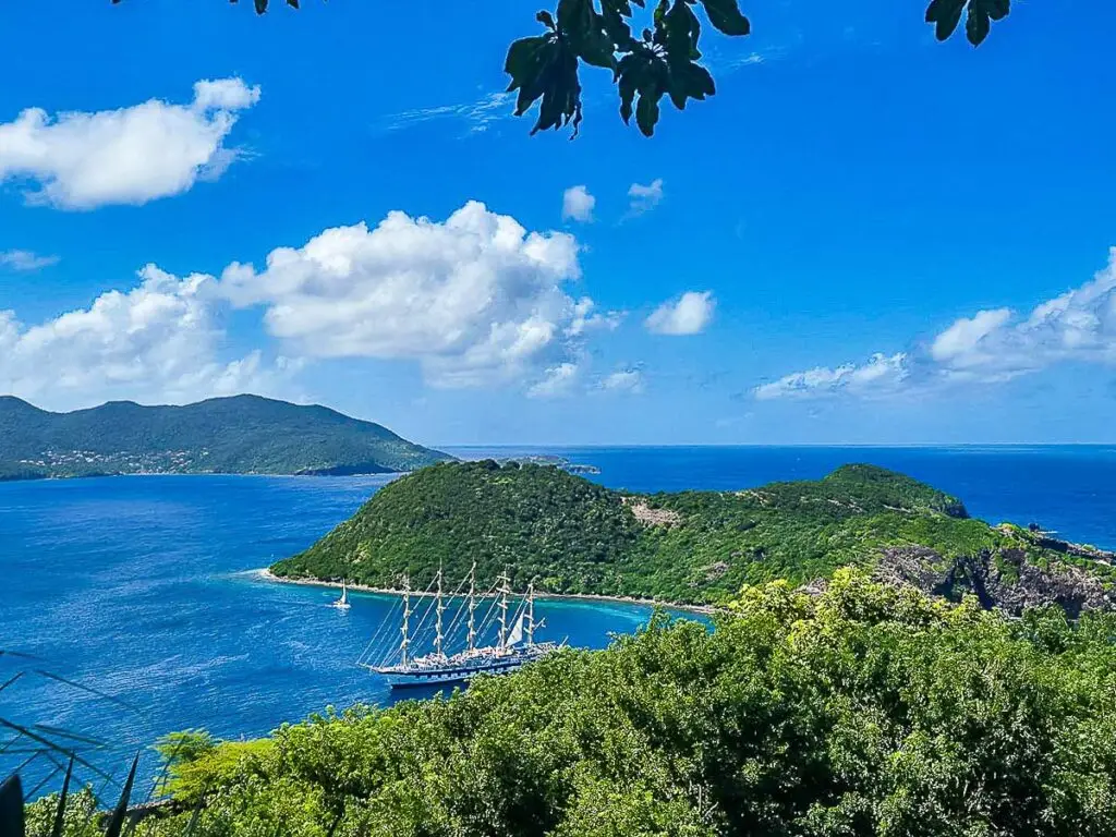Vue en hauteur sur la baie des Saintes depuis Terre-de-Haut, avec voilier à mâts multiples, mer turquoise et végétation tropicale