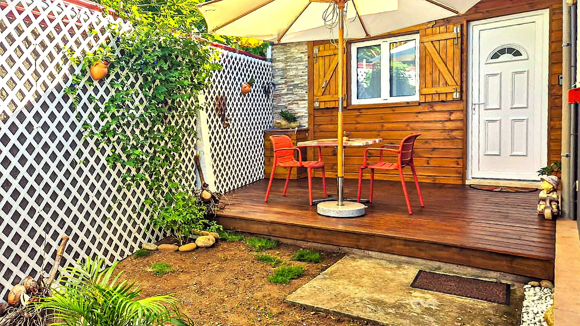 Terrasse privée du bungalow Chez Didine aux Saintes, avec mobilier rouge, parasol et ambiance végétale